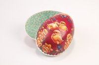 Húsvéti tojás (Dütni) színes papírmasé textil csíkborítással két félből, mindkettőn virágok közt 3 csirke. Belseje zöld apróvirágos tapétapapírral bevonva.